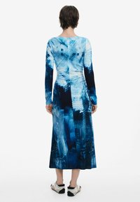 Haljina s dugim rukavima u nijansama plave boje s uzorkom gradskog krajobraza, strukirana u struku i pada do duljine do sredine lista. Glatki, rastezljivi materijal.