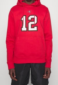 Roter Hoodie mit einer vorderen Kängurutasche, versehen mit einer großen schwarz-weißen "12" und einem kleinen Buccaneers-Logo auf der Brust. Weicher Stoff.