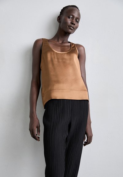 Top in satin marrone senza maniche con scollatura curvata, abbinato a pantaloni neri plissettati. Texture liscia, vestibilità rilassata e dettagli di cucitura minimi.