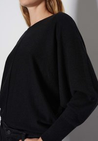 Maglione nero in morbido knit con scollo ampio, spalle scese e vestibilità comoda. Polsini a costine e cuciture minimali. Design testurizzato e casual.