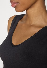 Black ribbed tank top featuring a deep V-neck design, with smooth texture and body-hugging fit. Close-up on neckline and shoulder.