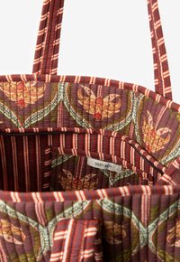 Sac fourre-tout matelassé avec un intérieur marron orné de motifs floraux en orange et vert, agrémenté de poignées à rayures rouges et blanches.