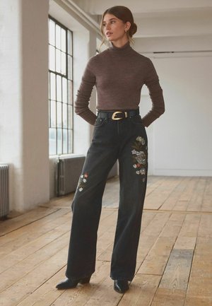 Zwarte wijde jeans met bloemenborduursel aan de voorkant en een zwarte riem met een gouden gesp, gecombineerd met een aansluitende bruine coltrui.