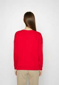 Felpa rossa con maniche lunghe, collo rotondo e polsini a costine. Realizzata in materiale morbido, presenta una vestibilità rilassata e un design semplice.