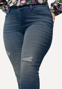 Mörkblå skinny jeans med slitna knäbleck, slät textur, figursydd design och femficksstil. Denimtyg med lätt nötthet.