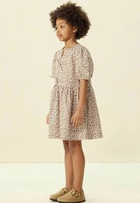 Braunes Leopardenmuster-Kleid mit Puffärmeln und Taillengürtel, kombiniert mit beigen Slippern. Das Kleid hat einen runden Ausschnitt und einen gerafften Rock.