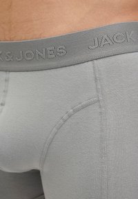 Close-up of a person wearing light grey boxer briefs with a grey elastic waistband branded "JACK & JONES."
