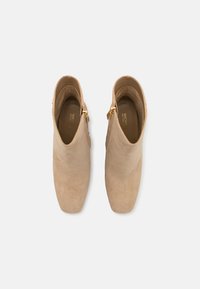 Beige ruskind ankelstøvler med spids tå, guld hardware lynlåsdetalje og en glat indvendig foring.