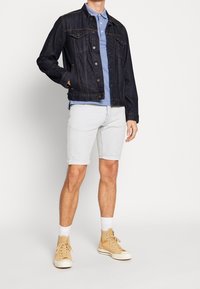Dark denim jacket with a collared blue polo shirt, light blue denim shorts, and beige high-top sneakers with white soles and socks.