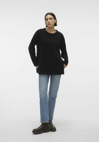 Maglione nero a maglia con maniche lunghe, colletto rotondo e fessure laterali. Abbinato a jeans a gamba dritta di color blu chiaro e stivaletti alla caviglia marroni scuri.