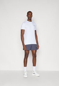 Λευκό κοντομάνικο μπλουζάκι, ναυτικές βερμούδες με λογότυπο, λευκά αθλητικά παπούτσια και λευκές κάλτσες. Απλό σχέδιο, ομαλή υφή, ουδέτερα χρώματα.