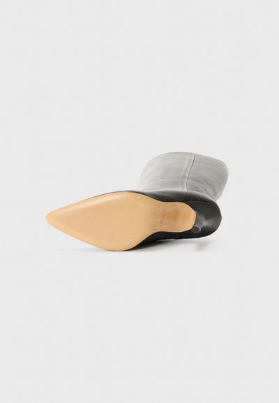 Svart och grå läderhögklackad stövel med spetsig tå och en beige sula. Har en slät textur och en sömlös ovandel.