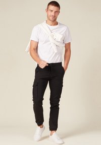 Zwarte cargo broek met meerdere zakken, taps toelopende benen en geribbelde boorden, gecombineerd met een eenvoudige witte T-shirt en witte sneakers.