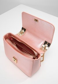 Růžová umělá kabelka s lesklým povrchem, zlatým kovovým uzávěrem a akcenty, a vnitřní kapsou na zip. Obsahuje řetízkový popruh.