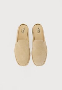 Svijetlosmeđi slip-on cipele od suède s okruglim vrhom i potplatom u stilu užeta. TOMS brendiranje vidljivo na ulošku.
