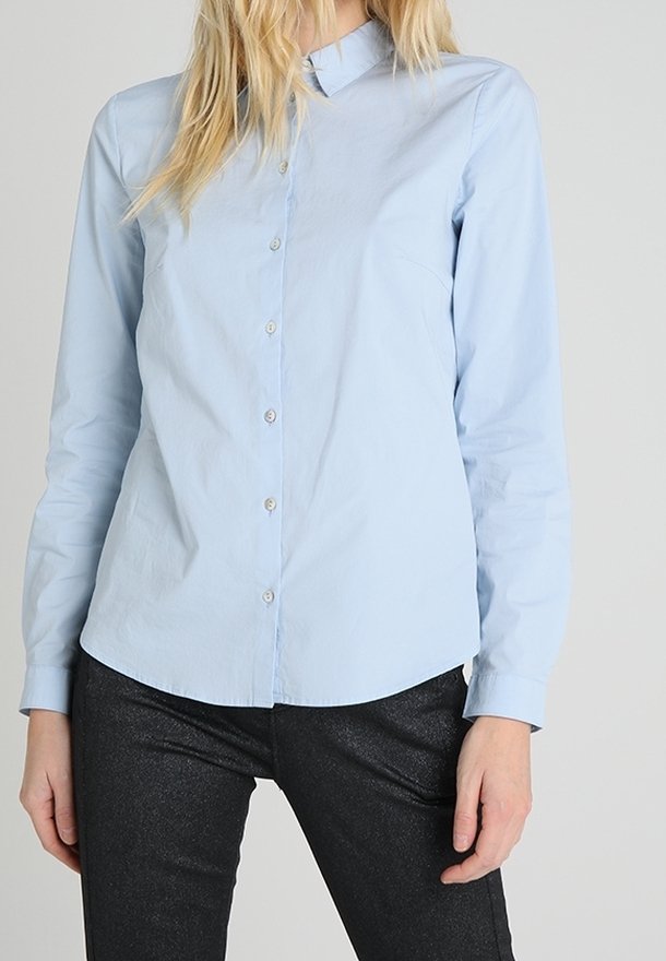 Chemise bleu clair à manches longues, coupe ajustée, avec un col et une texture lisse, accompagnée d'un pantalon sombre et brillant.
