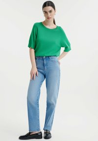 Zeleni kratki rukavi s majicom u kombinaciji s svijetloplavim trapericama visokog struka. Outfit je upotpunjen crnim loafers cipelama s pozlatnim detaljima.