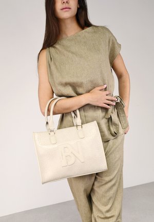 Bolso de mano color crema con el logo "BN" en relieve, superficie texturizada y asas dobles. Combinado con un atuendo holgado en tonos verdes apagados.