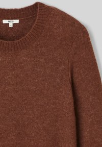 Pull en tricot marron avec un col rond côtelé, fabriqué à partir d'un tissu doux. La texture est légèrement duveteuse avec une teinte chaude et terrestre. Étiquette de taille visible.
