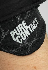 Un matériau textile noir présentant le texte "PURE CONTACT" en lettres blanches en gras. Le tissu a un motif texturé et un bord cousu.
