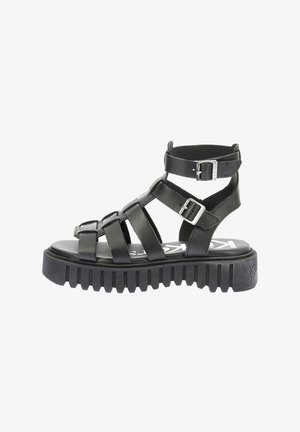 Zwarte leren sandaal met bandjes, voorzien van een stevige rubberen zool, meerdere kruisbandsluitingen en verstelbare enkelgespen.
