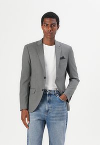 Grå dressjakke med notched lapels, to knapper og brystlomme. Brukt over en hvit t-skjorte og kombinert med lyseblå jeans.
