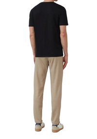Schwarzes T-Shirt mit kurzen Ärmeln kombiniert mit beigen Hosen. Der Stoff erscheint weich und hat ein Rundhalsausschnitt-Design. Das Outfit wird durch weiße Sneakers ergänzt.