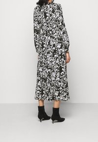 Musta kukkamekko, jossa valkoiset kukkakuviot, pitkät hihat, vyötärö nyöritetty ja midimittainen helma. Yhdistetty mustien nilkkureiden kanssa.