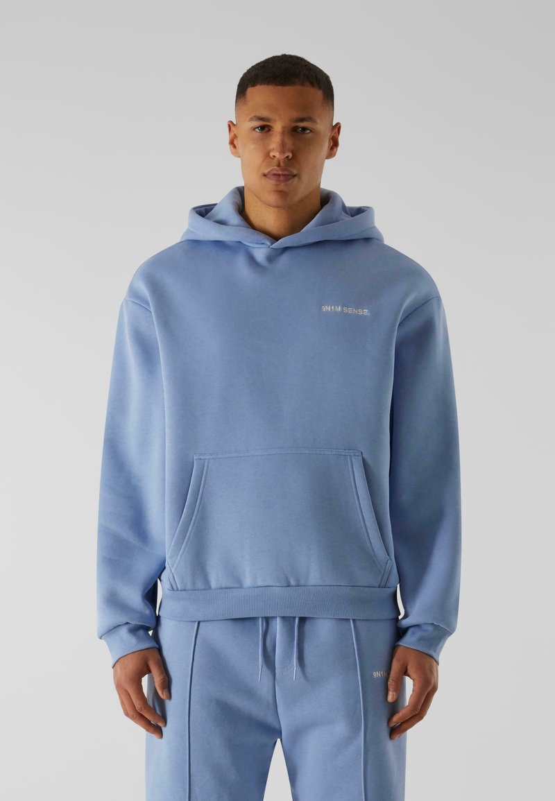 Lyseblå hoodie lavet af blød stof med en kengurulomme, ribbede manchetter og hætte med snorelukning. Har diskrete logodetaljer.