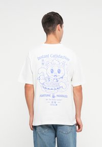 Witte katoenen T-shirt met een blauwe cartoonkat die noedels vasthoudt, met op de achterkant de tekst "Instant Catisfaction" en "Fortune Noodles".
