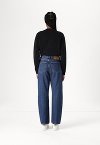 Sudadera negra con puños acanalados, combinada con jeans de mezclilla azul de cintura alta. Zapatillas blancas completan el conjunto. Diseño clásico y casual.