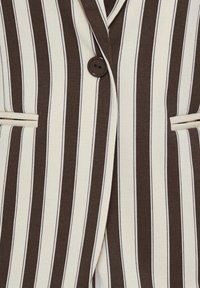 Gros plan d'un blazer à rayures verticales marron et crème avec un seul bouton marron foncé et deux poches horizontales fendues.