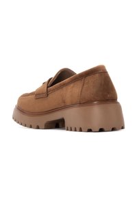 Mocasines de ante marrón con una suela de goma gruesa que presenta un patrón de textura antideslizante y sutiles detalles de costura en la parte superior.
