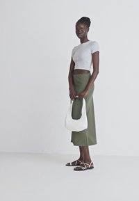 T-shirt gris court, jupe taille haute verte olive, sac à main blanc, et sandales à lanières. Design simple et épuré sans motifs.