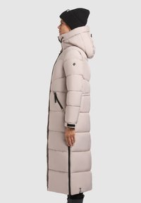 Dlhý, polstrovaný zimný kabát svetlo béžovej farby s vysokým golierom, zipsovými vreckami a odnímateľnou kapucňou. Mäkka látka s viditeľným šitím.
