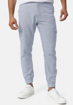 Hellblaue Cargo-Hosen mit elastischen Bündchen, ausgestattet mit Seitentaschen und einem strukturierten Stoff. Tragen mit weißen Turnschuhen.