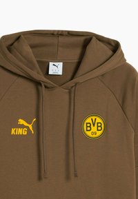 Brun hættejakke med gult Puma-logo og "KING" tekst til venstre, samt gult Borussia Dortmund "BVB 09" badge til højre.