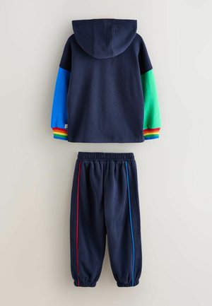 Tamsiai mėlynas džemperis su kapišonu, margintomis rankovėmis ir ribotais rankogaliais. Atitinkamos tamsiai mėlynos kelnės su raudonomis ir mėlynomis šoninėmis juostelėmis. Minkštas medvilnės mišinys.