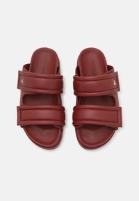 Rote Rutsche-Sandalen aus glattem synthetischen Material, mit zwei breiten Riemen und einem geformten Fußbett. Auffälliger goldener Hardware-Akzent an der Seite.