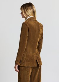 Blazer en velours côtelé marron avec une finition légèrement texturée, coupe croisée simple, revers crantés et quatre boutons décoratifs sur les manches.
