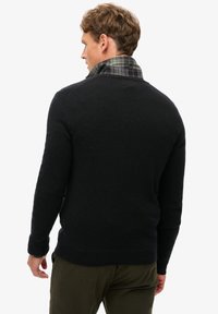 Zwarte gebreide trui met een gestructureerde afwerking, voorzien van een geruite kraag in groen en blauw, aansluitend ontwerp en geribbelde mouwen aan de onderkant.
