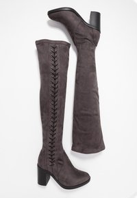 Botas de ante gris por encima de la rodilla con un tacón ancho y un cordón decorativo a lo largo del lado exterior. Textura suave con punta redondeada.