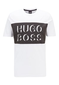 Krátký rukáv tričko v bílé a tmavě šedé barvě, které má odvážný nápis "HUGO BOSS" přes hruď, kulatý výstřih a volný střih.