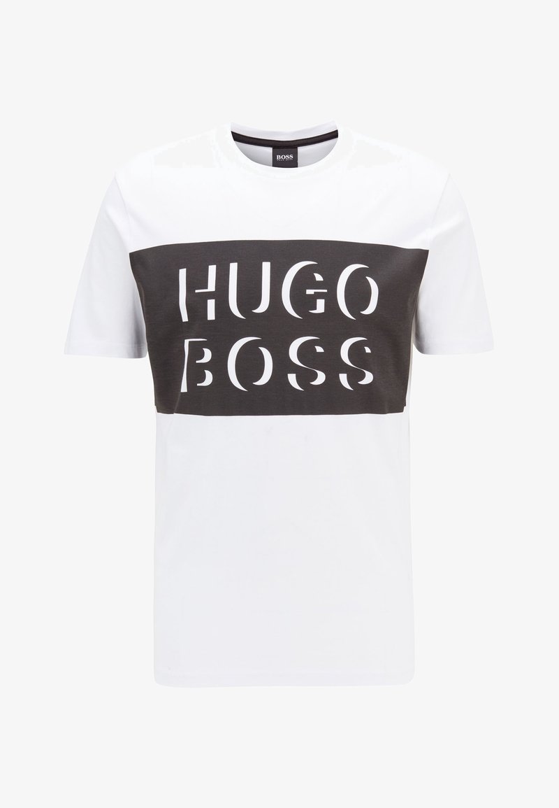 Krátký rukáv tričko v bílé a tmavě šedé barvě, které má odvážný nápis "HUGO BOSS" přes hruď, kulatý výstřih a volný střih.