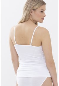 Top aderente bianco con spalline sottili regolabili, realizzato in morbido misto cotone, caratterizzato da una texture liscia e un taglio all'altezza dei fianchi.