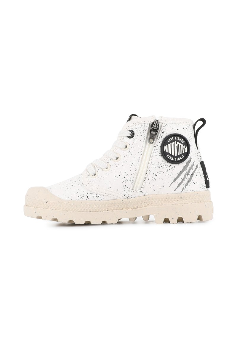 Baskets montantes blanches avec des éclaboussures noires, semelle beige, fermeture éclair sur le côté, lacets et un patch circulaire noir avec le logo Palladium sur la cheville.
