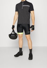 Jersey de ciclismo de manga corta en negro y gris con cremallera y detalles estampados, combinado con pantalones cortos acolchados negros con toques en neón. Un casco negro y zapatillas de ciclismo completan el conjunto.