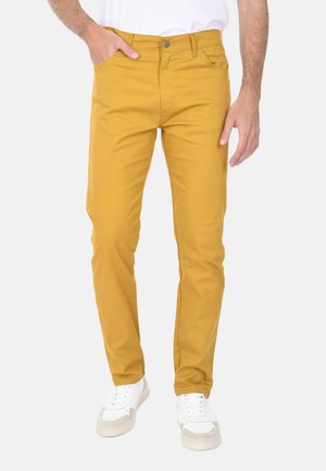 Chino in cotone giallo a vestibilità slim, con tasche frontali e chiusura a bottone, indossati con sneakers bianche.