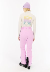 Roze skibroek met zwarte accenten, gecombineerd met een lichtgekleurde langslavende top met een kleurrijke bergafbeelding op de achterkant.