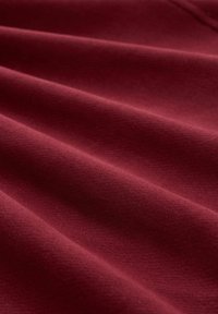 Tessuto borgogna con una superficie liscia, drappeggiato con pieghe visibili e sottili variazioni di tonalità, con una finitura morbida e opaca.